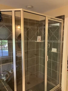 Old shower with sliding glass doors and worn tile