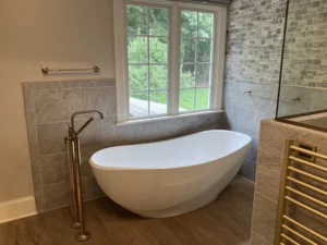 Freestanding tub beneath large window with stone accent wall